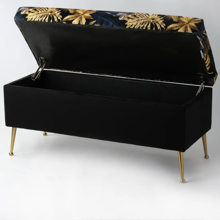 Elegante puf de almacenamiento negro con tapizado de hojas sobre patas de metal dorado.