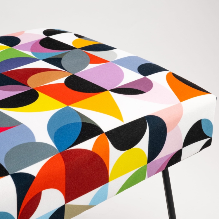 Banco tapizado con estampados coloridos y patas en forma de alfiler